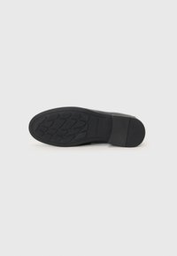 Black rubber sole with textured tread for grip, angled heel, smooth finish, and minimal branding.  Clean, modern design.