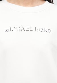 Λευκό φούτερ με στρογγυλή λαιμόκοψη, διακοσμημένο με ανάγλυφο κείμενο "MICHAEL KORS" σε αντίθετη απόχρωση, με λεία υφή και μοντέρνο σχέδιο.