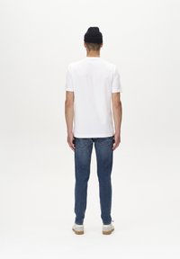 Weißes T-Shirt mit kurzen Ärmeln und rundem Ausschnitt, kombiniert mit blauen Denim-Jeans. Das Model trägt außerdem eine dunkelmarinefarbene Strickmütze.