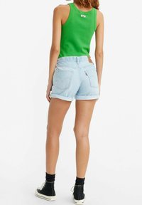 Vihreä hihaton paita, vaaleat farkkukäärepöksyt takataskuilla, farkkutagi vyötäröllä ja mustat korkeavartiset tennarit valkoisilla pohjilla.