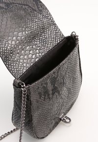 Harmaa teksturoitu nahkainen käsilaukku, jossa on ketjuhihna, läpällinen suljin ja vuoraamaton sisäosa. Ulkopuolella erottuva käärmemäinen kuvio.