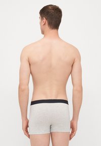 Graue Boxer-Briefs mit einem schwarzen Bund, aus glattem, elastischem Stoff und in einer engen Passform, von hinten betrachtet.