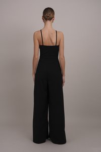 Tuta nera con corpetto aderente, spalline sottili e gambe ampie. Chiusura con zip sul retro e tessuto morbido e testurizzato.
