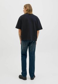 Zwarte korte mouwen T-shirt met een losse pasvorm, gecombineerd met blauwe spijkerbroek. T-shirt heeft een minimaal logo op de achterkant en een soepele textuur.