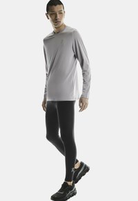 Ljust grå långärmad träningsöverdel, svarta leggings och svarta löparskor med texturerade sulor. Innehåller logotypdetaljer på tröjan och leggings.