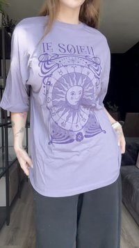 Lavanda majica s grafikom purpurne sunca s složenim dizajnom i tekstom "LE SOLEIL". Labav kroj s polu-dužinom rukava.