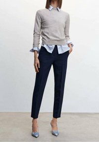 Beige svetr vrstvený přes světle modrou košilovou košili, doplněný o tmavě modré kalhoty na míru a světle modré lodičky s mašlovými detaily.