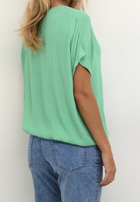 Løs fit mintgrøn top med korte ærmer, lavet af krøllet stof, parret med lyseblå denim jeans.