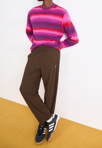 Flerfärgad randig tröja i rosa, lila och röd, i kombination med texturerade bruna byxor och svarta sneakers med vita ränder.