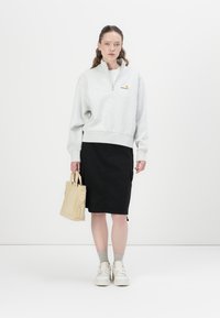 Grå fleece genser med kvart glidelås og ribbestrikket kant, kombinert med svart knelangt skjørt og beige lerrets totebag. Hvite sneakers og grå sokker.