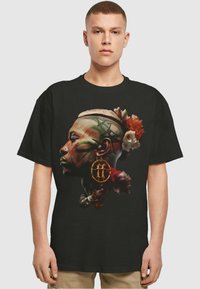 Svart t-skjorte med et fargerikt grafisk trykk av en profil med blomsteraksenter, intrikate mønstre og et ornament. Korte ermer, avslappet passform.