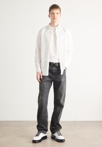 Biała koszula na guziki na białej koszulce, zestawiona z ciemnymi dżinsami i czarnymi butami z białymi akcentami. Gładkie tekstury i czyste linie.