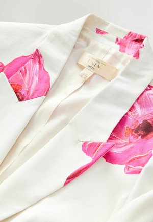 Leinenblazer mit großen rosa Blumenmotiven auf den Schultern und Taschen, in einer cremefarbenen Grundfarbe und mit glatter Textur.