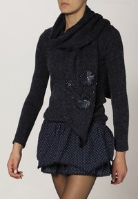 Námořnický pletený svetr s lodičkovým výstřihem a asymetrickým lemem, zdobený květinovými aplikacemi a korálky, kombinovaný s sukní s puntíky.