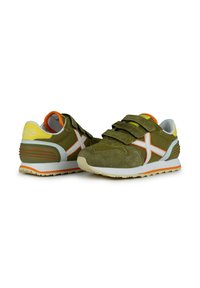 Zapatillas deportivas verdes que combinan materiales de malla y ante, con correas de Velcro, acentos naranjas y una suela de goma texturizada.