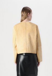 Veste en cuir jaune texturé avec un design court, présentant un col rond et des manches longues, associée à une jupe en cuir noire.