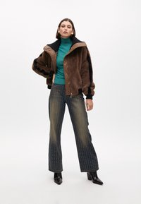 Brown shearling jacket with black accents, teal turtleneck sweater, flared denim jeans with gold dot patterns, and black pointed-heel boots.