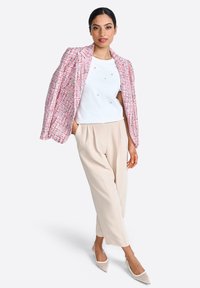 Vaaleanpunainen tweed-takki, jossa on teksturoitu muotoilu, valkoinen paita koristeilla, beige housut ja vaaleat kengät, joissa on kapea varvas.