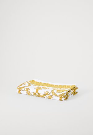 Presavijena bijela tkanina s detaljnim zlatnim uzorkom duž ruba, glatke teksture i čistih, ravnih nabora.