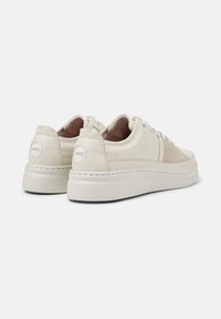 Cremefarbene Sneakers mit glatter Textur, minimalistischer Gestaltung und dicker Sohle, von hinten im Winkel dargestellt.