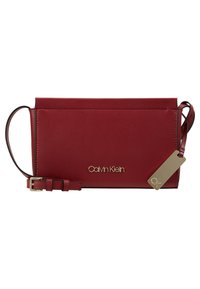Prostokątna czerwona skórzana torba na ramię z regulowanym paskiem oraz złotym logo Calvin Klein i metką z przodu.