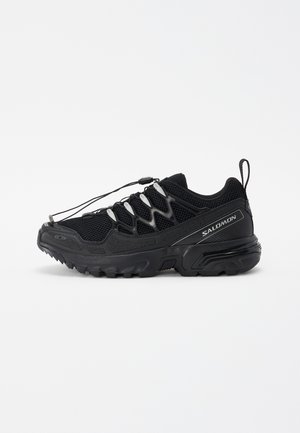 Baskets de course noires avec une tige en mesh, accents réfléchissants et lacets élastiques. Présente une semelle robuste avec des motifs de traction pour la stabilité.