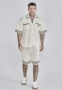 Hvid mesh kortærmet skjorte med brune detaljer og matchende shorts. Har to lommer og knaplukning foran. Bruges med hvide sneakers.