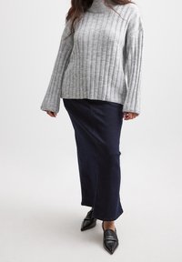 Grauer gerippter Pullover mit hohem Kragen, kombiniert mit einem dunkelblauen Jeansrock. Schwarze spitz zulaufende Schuhe runden das Outfit ab.