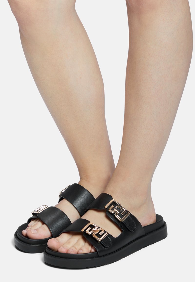 Black slide sandals with two wide straps, featuring metallic gold buckles. Thick sole with textured tread for grip. Smooth leather material.