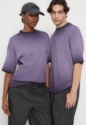 Du modeliai dėvi derančius trumpomis rankovėmis violetinės spalvos palaidus megztinius ir tamsiai pilkas kelnes, vienas modelis dėvi pilką kepuraitę ir kabančius auskarus.