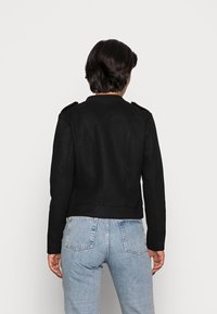 Giacca nera in misto lana con un design strutturato, spalline sulle spalle e una vestibilità corta, abbinata a jeans azzurri a vita alta.