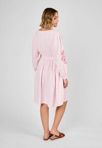 Rochie din bumbac roz, lungime până la genunchi, cu mâneci lungi și talie elastică; are broderie florală pe mâneca stângă și un material texturat.