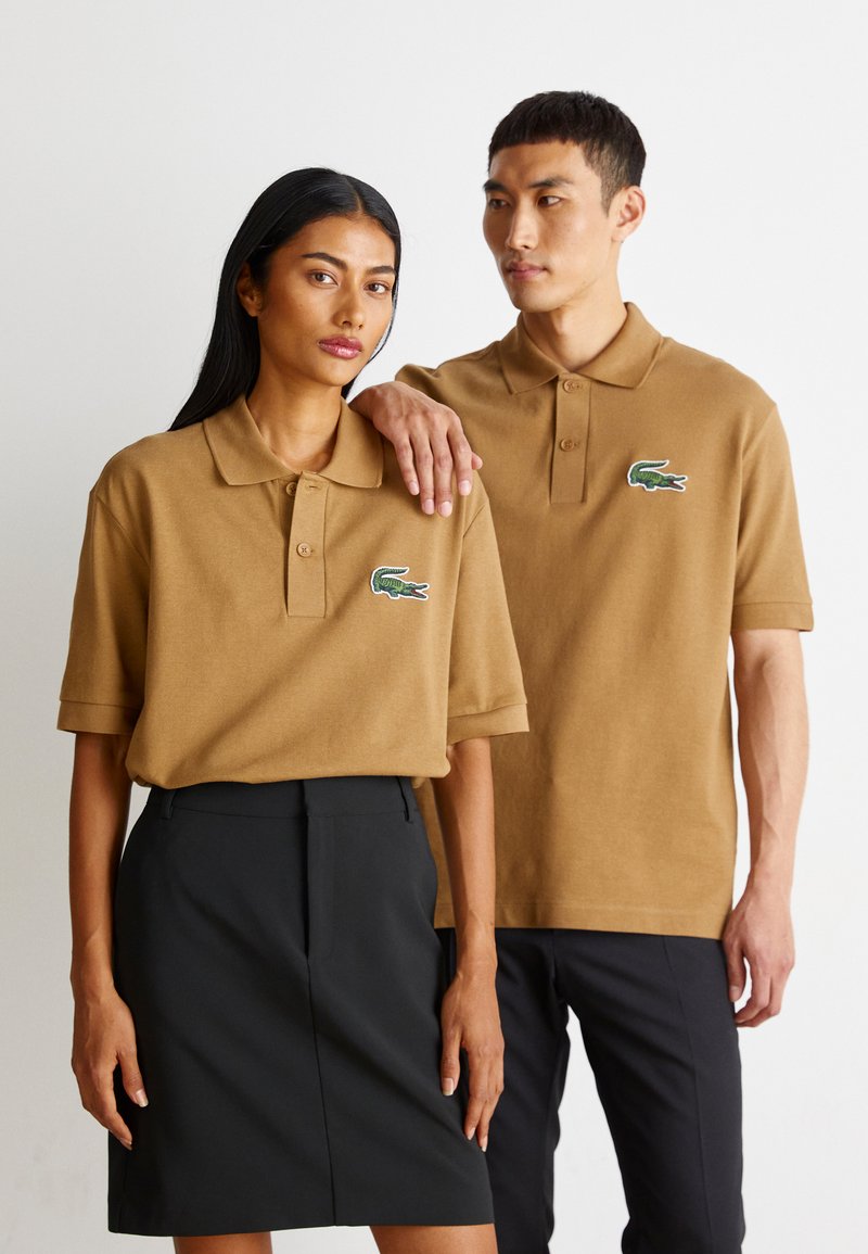 Ruske pohodne polo majice s zelenim logotipom krokodila, uparene s crnom olovkom suknjom i tamnim hlačama, nose ih dva modela.