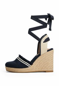 Navy canvas wedge sandal with textured espadrille heel, decorative stripes, open toe, and crisscross ankle ties. Natural fiber accents.