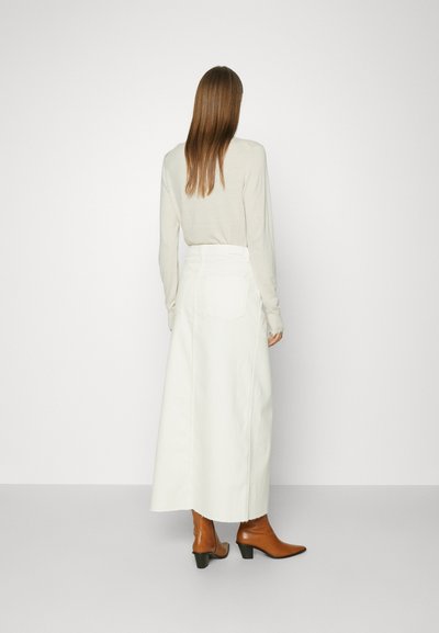 Lang witte rok met een hoge taille en zijzakken, gecombineerd met een lichtbeige top en bruine enkellaarzen met een puntneus.