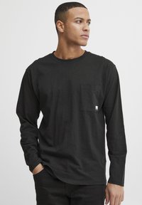 Black long-sleeve t-shirt made of soft fabric, featuring a chest pocket and a rounded hem. Simple design with minimal accents.
