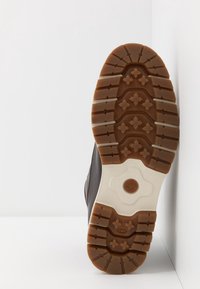 Suela de bota de goma marrón con un patrón de banda de rodadura texturizado. Acentos de marrón claro y una entresuela blanca. Diseño limpio y minimalista.
