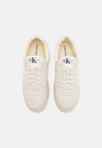 Sneakers in tela Calvin Klein di colore bianco sporco con una tomaia texturizzata, punta tonda, chiusura con lacci e una suola simile al sughero. Design leggero.