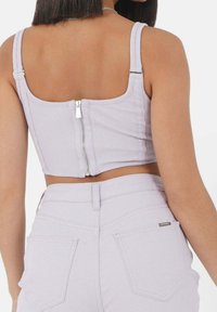 Top corto de canalé en color lila con tirantes ajustables y cierre con cremallera en el centro de la parte posterior. Combinado con pantalones de cintura alta a juego.