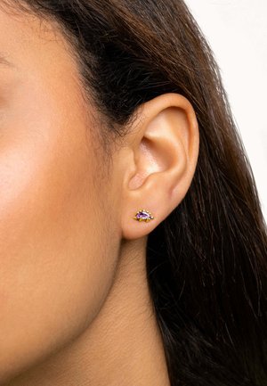 Orecchino a bottone in oro con una gemma viola circondata da piccoli accenti bianchi, su uno sfondo di capelli scuri.