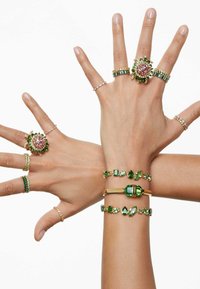 Collection of rings and bracelets featuring green and pink gemstones set in gold and silver tones, with intricate designs and varied textures.