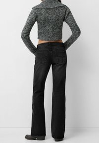 Jeans negros acampanados combinados con un suéter de punto gris recortado que presenta un cuello amplio. Textura suave y bolsillos estándar en la parte trasera.