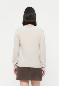 Ljusbeige tröja med långa ärmar och rund hals, kombinerad med en brun kordjetkjol, sedd bakifrån mot en vit bakgrund.