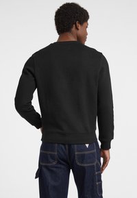 Felpa nera a girocollo con maniche lunghe, polsini e orlo a coste, realizzata in tessuto morbido; abbinata a jeans cargo blu scuro con tasche.