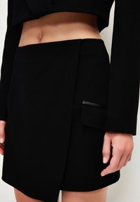 Falda larga negra con una textura suave, que presenta un pequeño bolsillo lateral y un diseño ajustado que se sitúa por encima de la cintura.