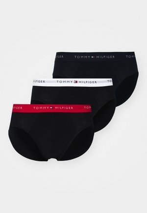 Tri parov moških spodnjic, ki imajo črno tkanino, elastične pasove v rdeči, beli in črni barvi z logotipom "TOMMY HILFIGER". Gladka tekstura.