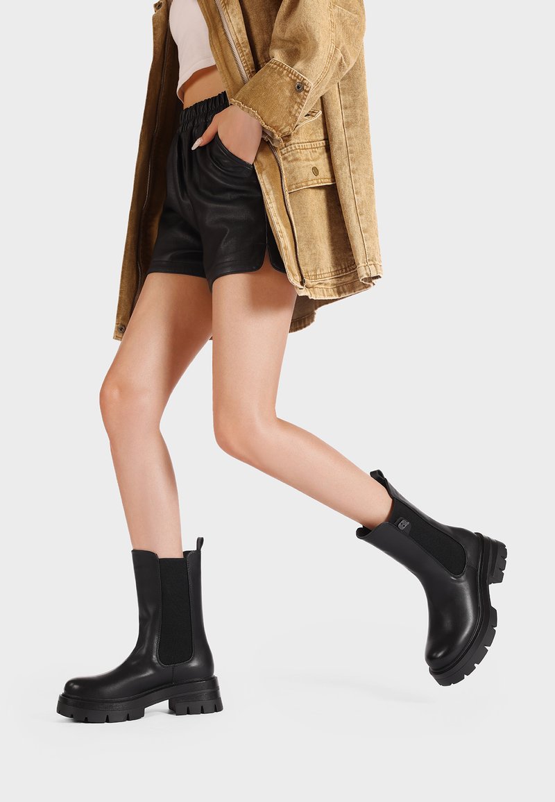 Stivaletti neri in pelle con pannelli elasticizzati laterali e suole in gomma spessa. Design elegante con un tirante sul retro per indossarli facilmente.