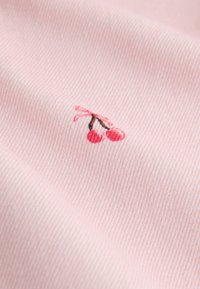 Tissu rose avec un petit motif brodé de deux cerises rouges et des tiges marron attachées avec un nœud rose.