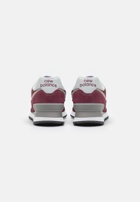 Le sneakers New Balance da uomo presentano una tomaia in suede bordeaux con accenti bianchi, colletto imbottito e un tallone a strisce grigio e bianco.