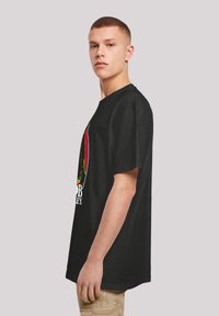 Black short-sleeve t-shirt featuring a graphic design with yellow, red, and green accents. Loose fit with a round neckline and casual style.